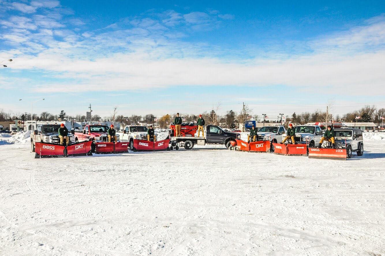 A row of snow plows parked on a snowy surface, ready for winter road maintenance.